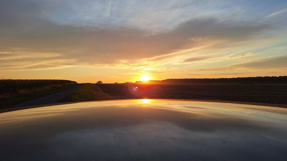 Orangefarbener Sonnenuntergang spiegelt sich in glatter Fläche 