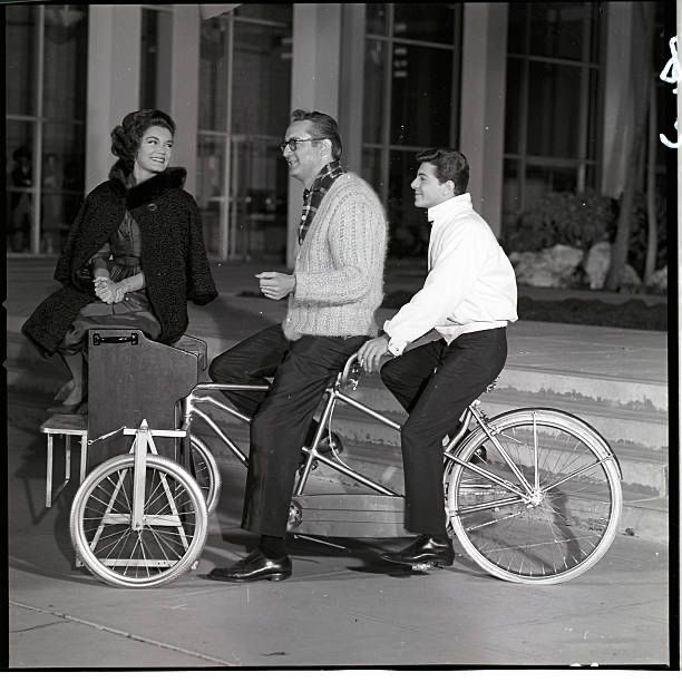 Photo of a woman and two men on a tandem tricycle with a piano mounted on the front end. The woman is sitting on the piano and the men are resting astride the bike. It’s from an episode of The New Steve Allen Show called Campus U.S.A., which aired December 27, 1961.
