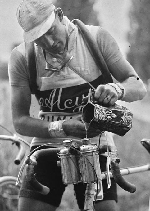 Photo of a bicycle racer pouring water from a pitcher into one of two bidons mounted on the handlebars of his bike. The pitcher has been identified as a Frie Onnaing majolica pitcher.
