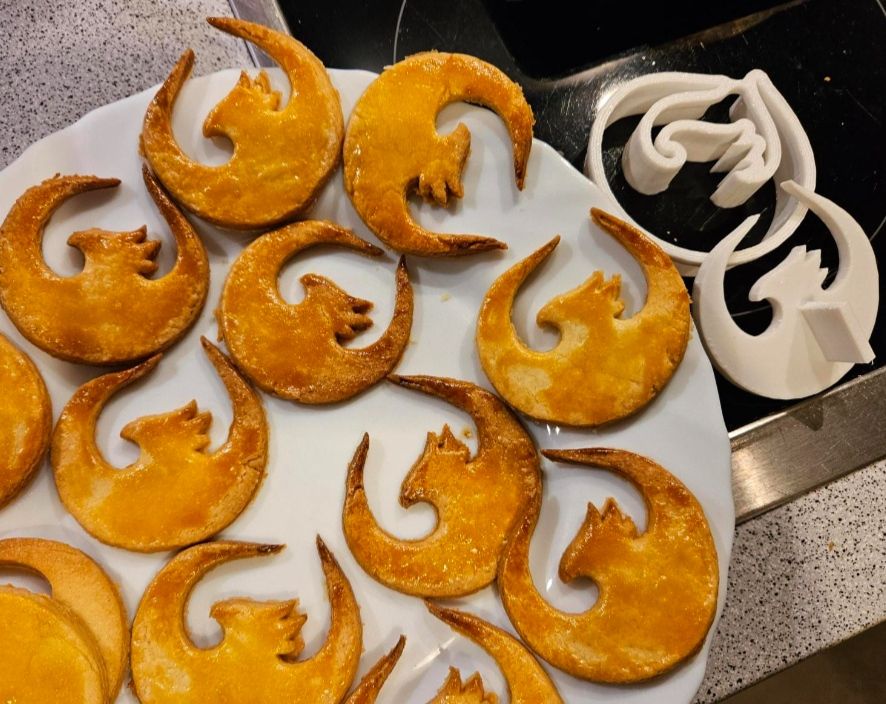 Christmas cookies in the shape of the UI5 logo phoenix and a 3D-printed cookie cutter in the same shape, along with a kind of also 3D-printed press stamp for pressing out the dough without ripping off the phoenix' wings