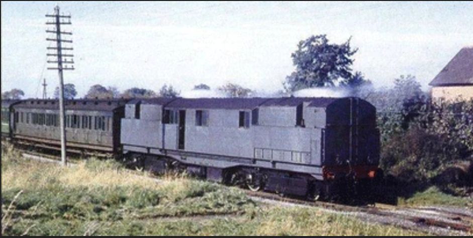 color photo of the CC1 locomotive designed by oliver bulleid for the irish railways. it has a central cab and a long nose on each side. it is pulling a train of old passenger cars through the countryside