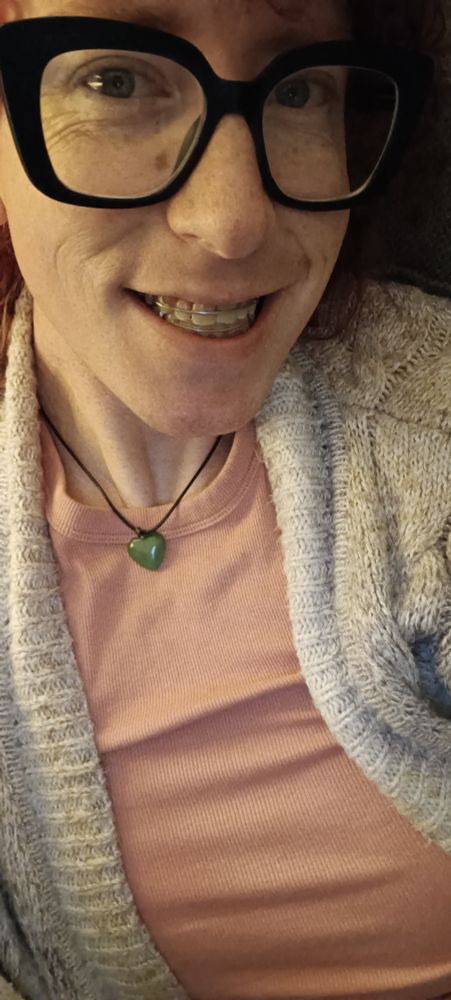 Ripley in a salmon tank, and tan cardigan, smiling, showing her retainers