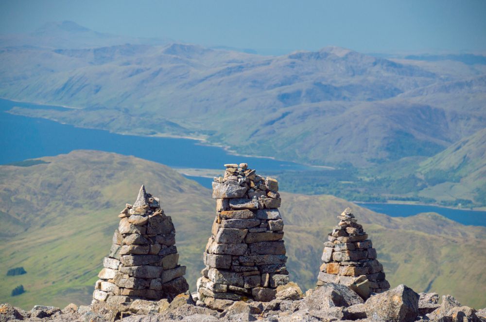 Three cairns looking over green hills and lochs.