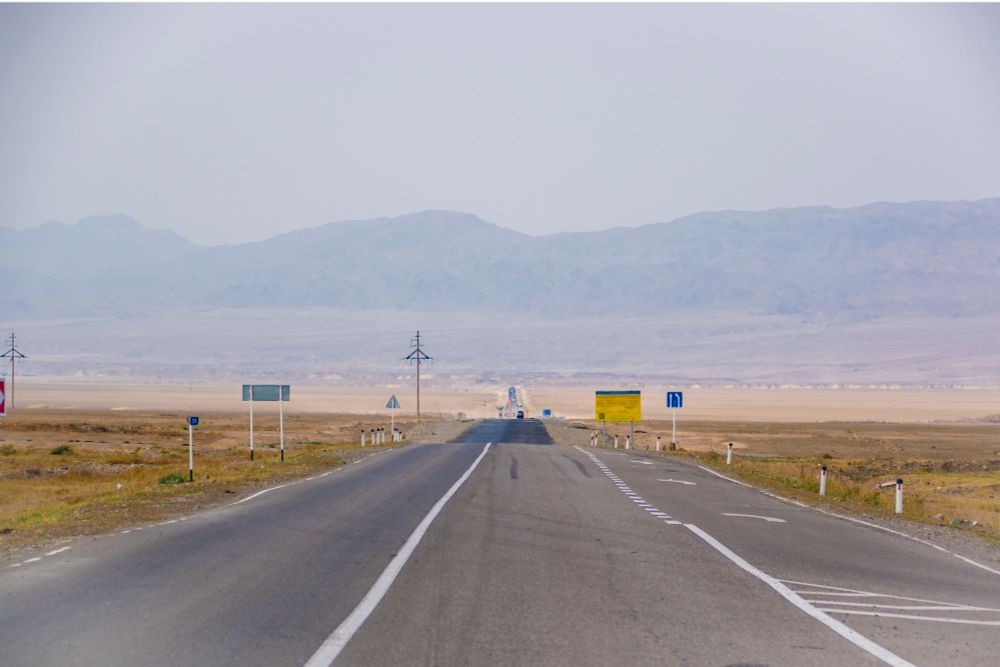 A long straight road follows every bump and contour of the landscape to a vanishing point.