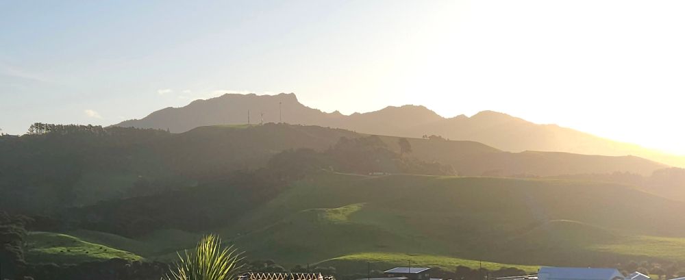 Mountain at sundown behind green hills