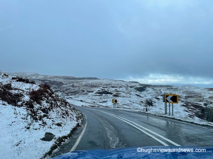 A photo of a wet road with a slight snowfall on either side of the road. 
