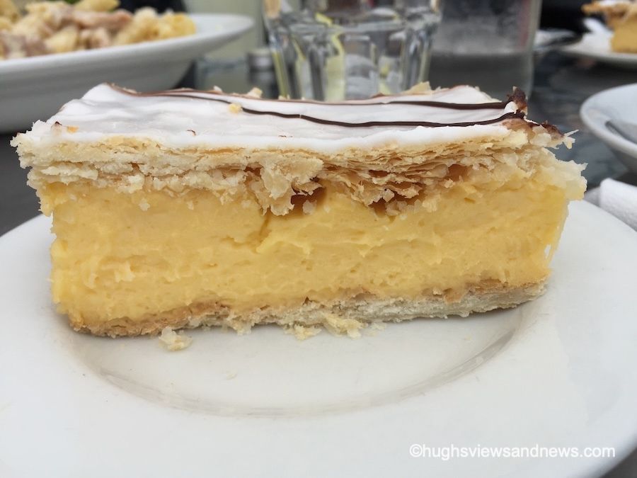 A photograph of a close-up of an iced-custard slice sitting on a white plate. 