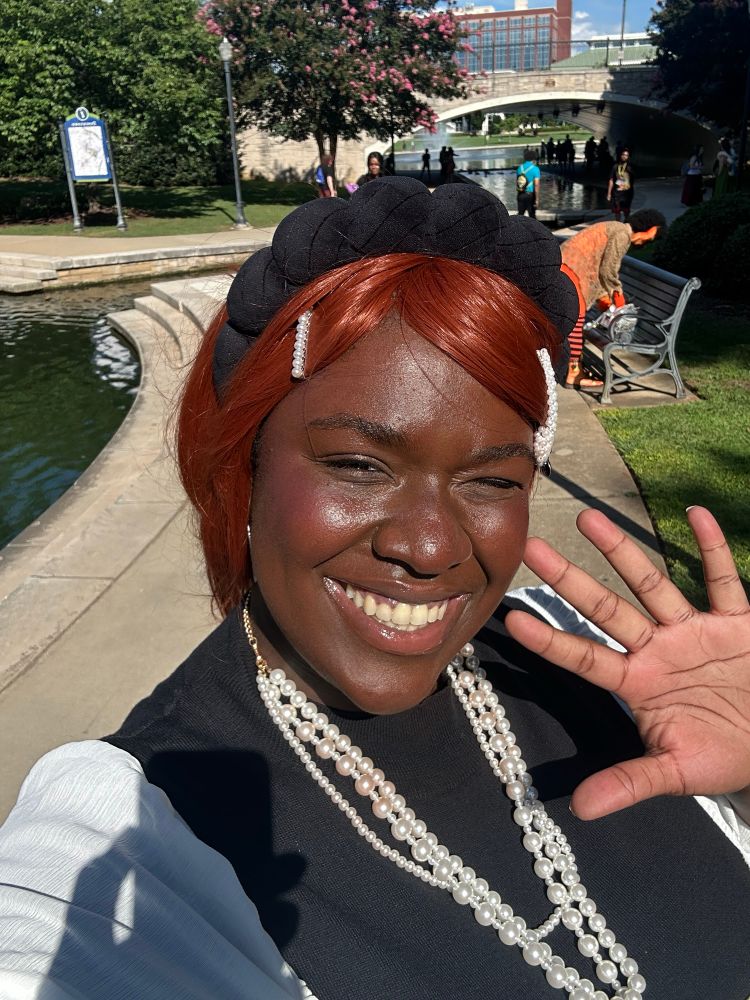 kristaliizecos gives a bright smile into the camera for a selfie cosplaying as Nana “Hachi” Komatsu. Their hand is near their face palms open to the camera for a cute pose.