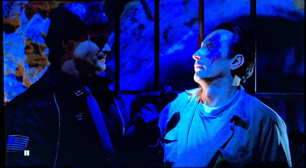 Alex Kubik (right) as convict 'Face' has a staredown with deputy Billy Williams in an old mineshaft, he wears a prison uniform, has slicked back hair & a distinctive purple birth mark adorns one side of his face. His body language exudes oily arrogance.