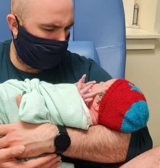 Man and newborn baby. Baby wearing a red and light blue hat, in hospital
