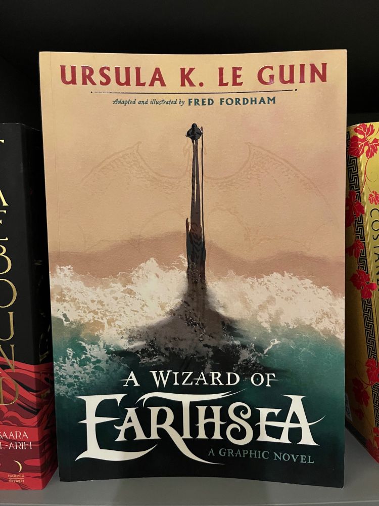 An image of the front cover of A Wizard of Earth sea, graphic novel. The cover depicts a shadowy form rising from a stormy sea. In certain lights, you can see the form of a dragon where the shadow is, 