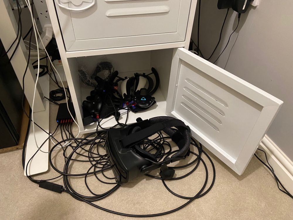 A VR headset with trackers and controllers inside a cabinet with a mess of cables.