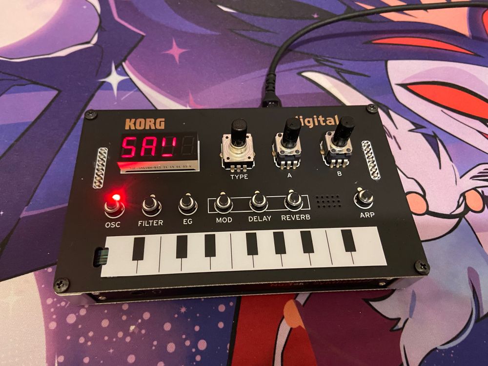 A Korg NTS-1 digital synthesizer, comprised of several dials, buttons, and small keyboard strip.