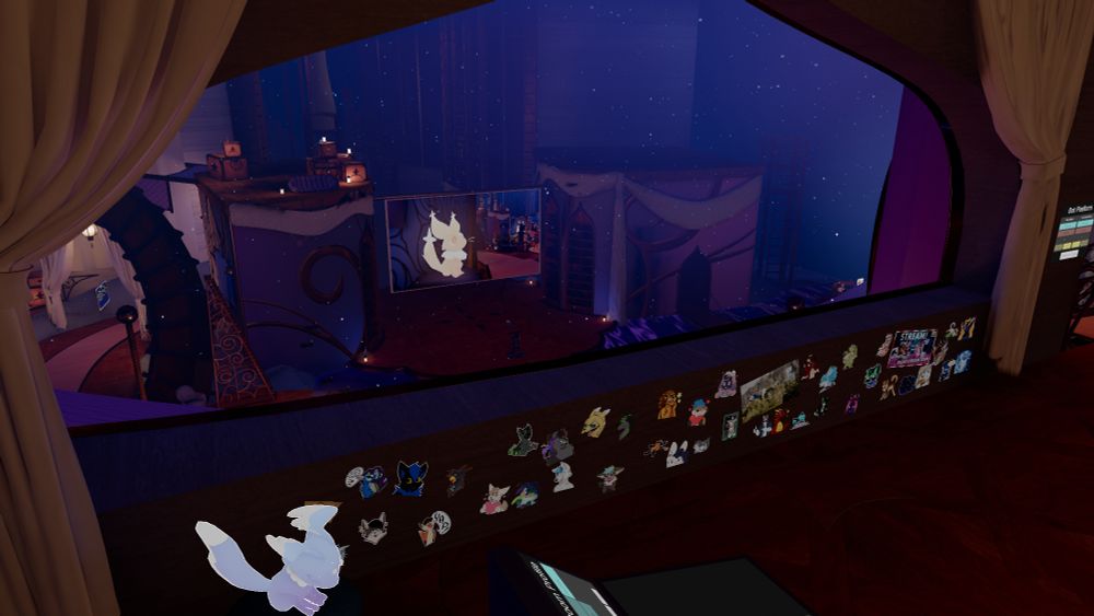A look out from the control booth to the stage. The wall below the window is covered in stickers of team members, and a dream creature sleeps to one side.