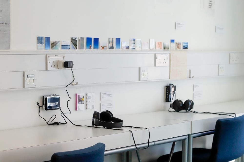 An installation of very small photos lined up on a shelf along with walkman cassette players and headphones.