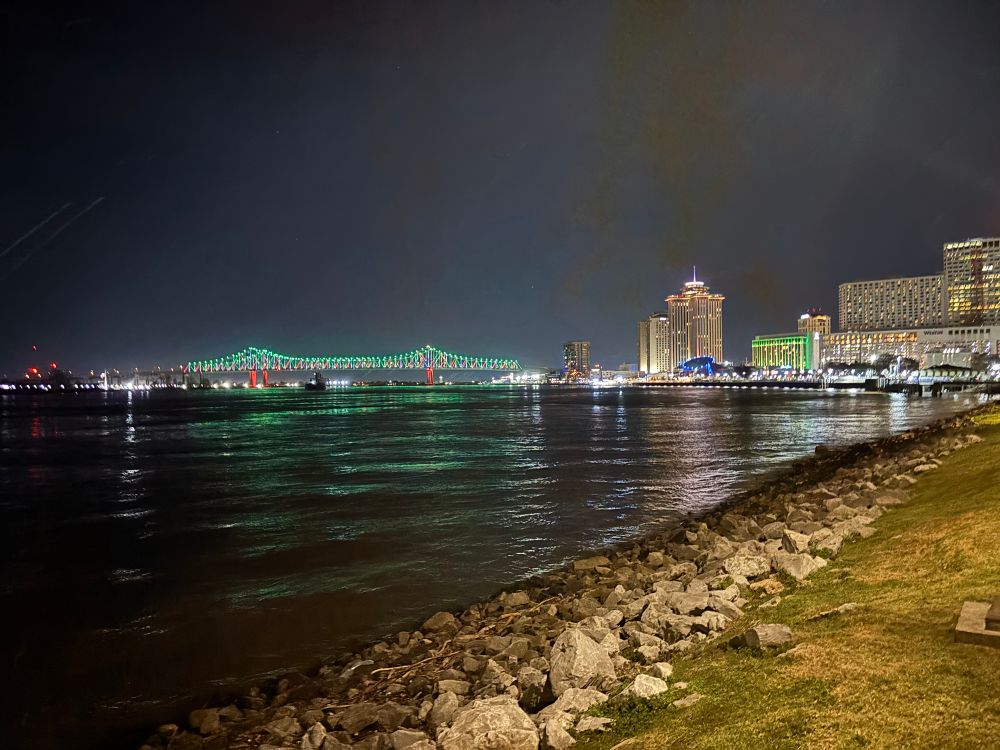 New Orleans skyline at night by the waters edge. Dotted with the bridge and building lit in green.