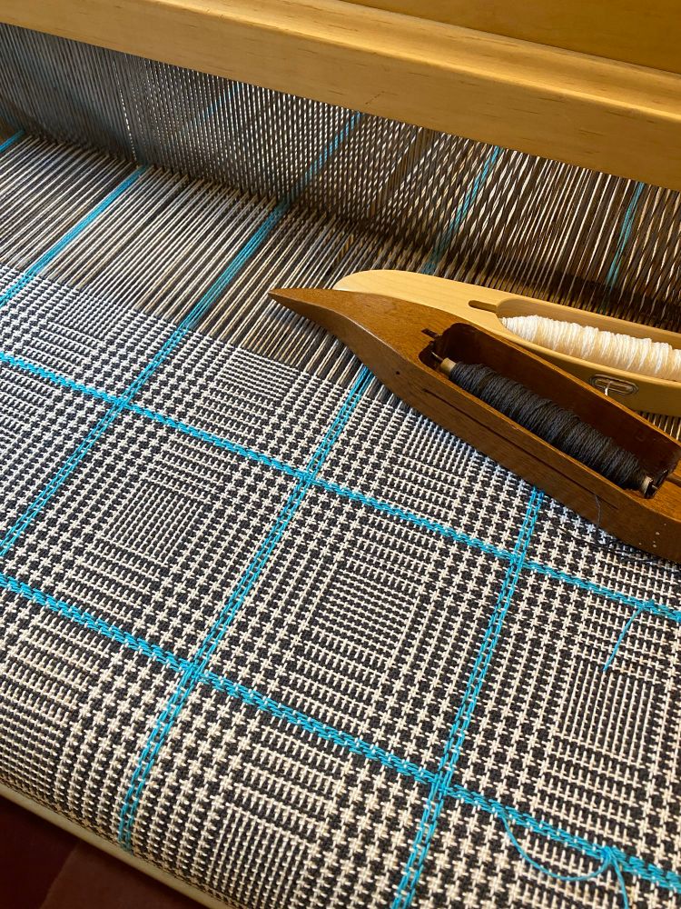 Black and white fabric in loom with small color and weave checks and a turquoise overcheck 