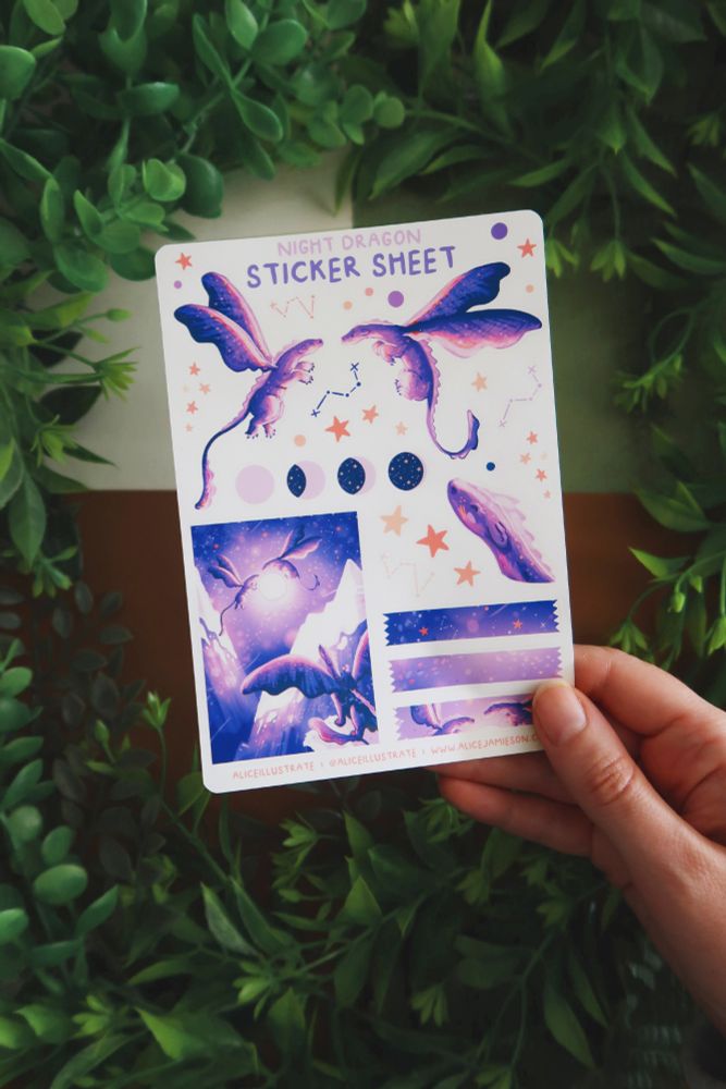 A hand holding a sheet of dragon stickers. They are purple with stars in their wings. Some of the stickers are of dragons, there's also stars, moons and cut tape shapes and a miniature piece of dragon artwork as a sticker too.
