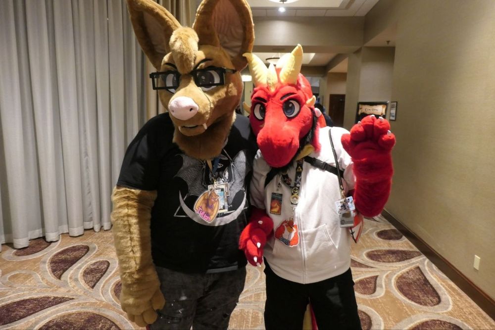 A married gay couple of furries in suit, one a brown vampire bat and the other a red Welsh dragon 
