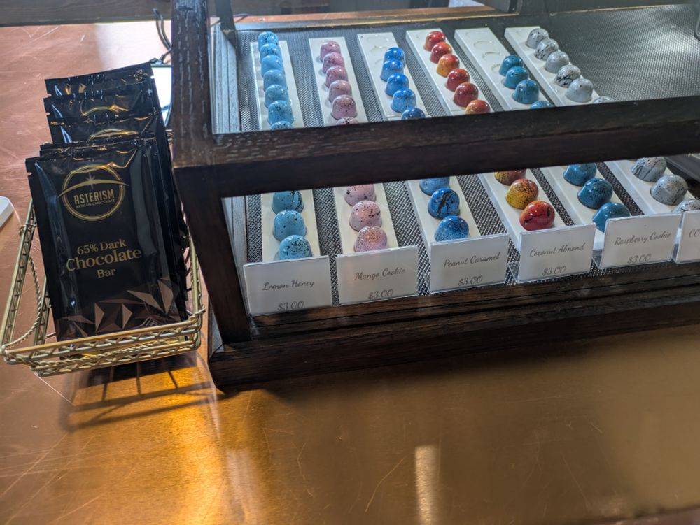 The bonbons in a glass display next to dark chocolate bars for sale