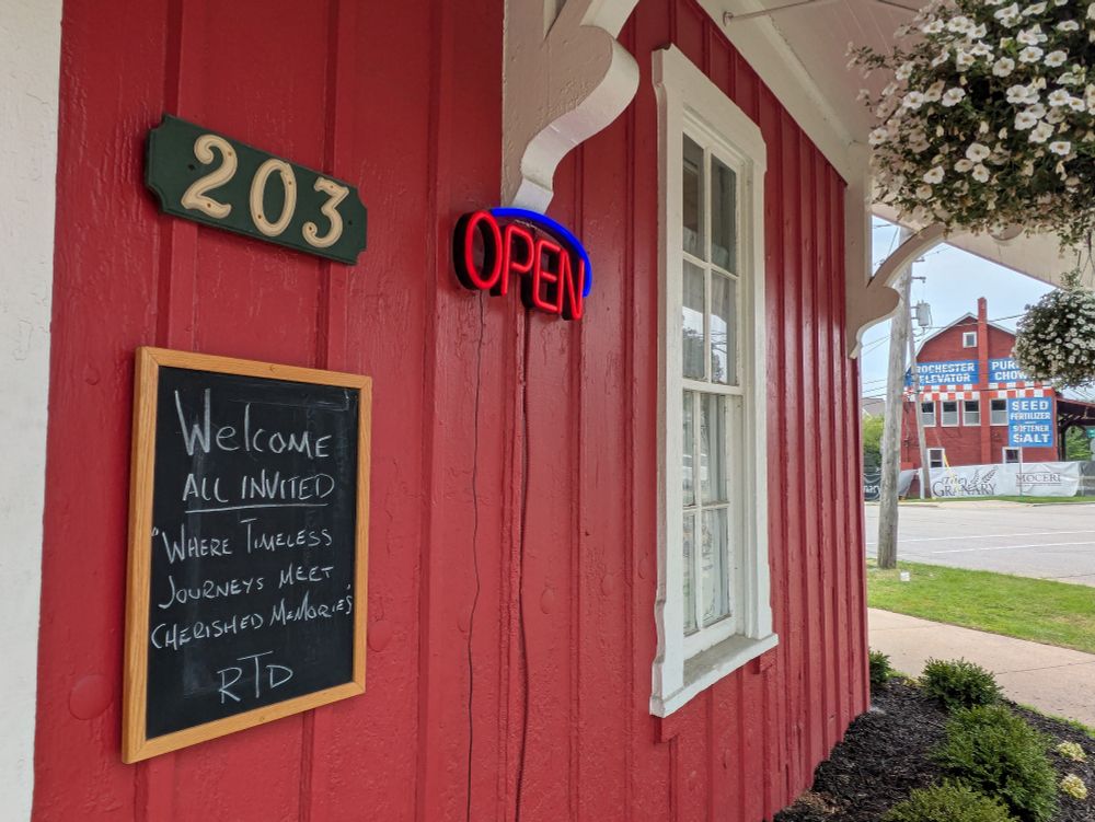 Chalkboard sign outside the front door reads, "Welcome. All Invited. Where timeless journeys meet cherished memories – RTD" (Rochester Train Depot)