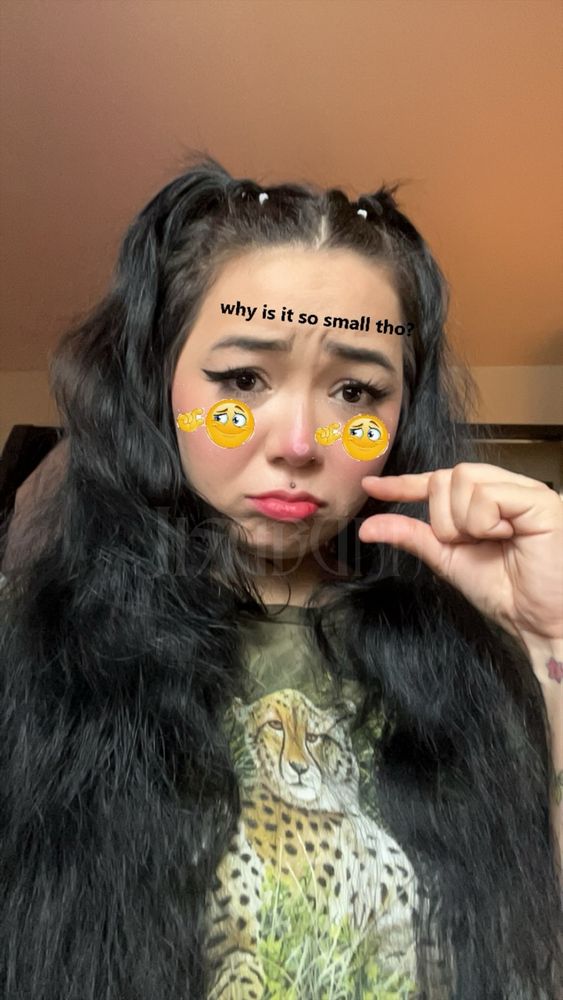 Jisu with super long black wavy hair in half up half down pigtails, using an emoji filter that says “why is it so small tho” and pinching their fingers close together to symbolize something being small. They are slightly pouting.