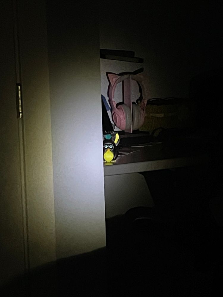 A Furby, peaking around the corner, perched on a desk.