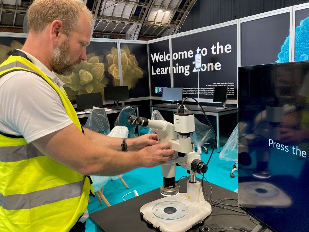 A staff mmber in a yellow hi-vis vest sets up a microscope on a desk in the RMS Learning Zone