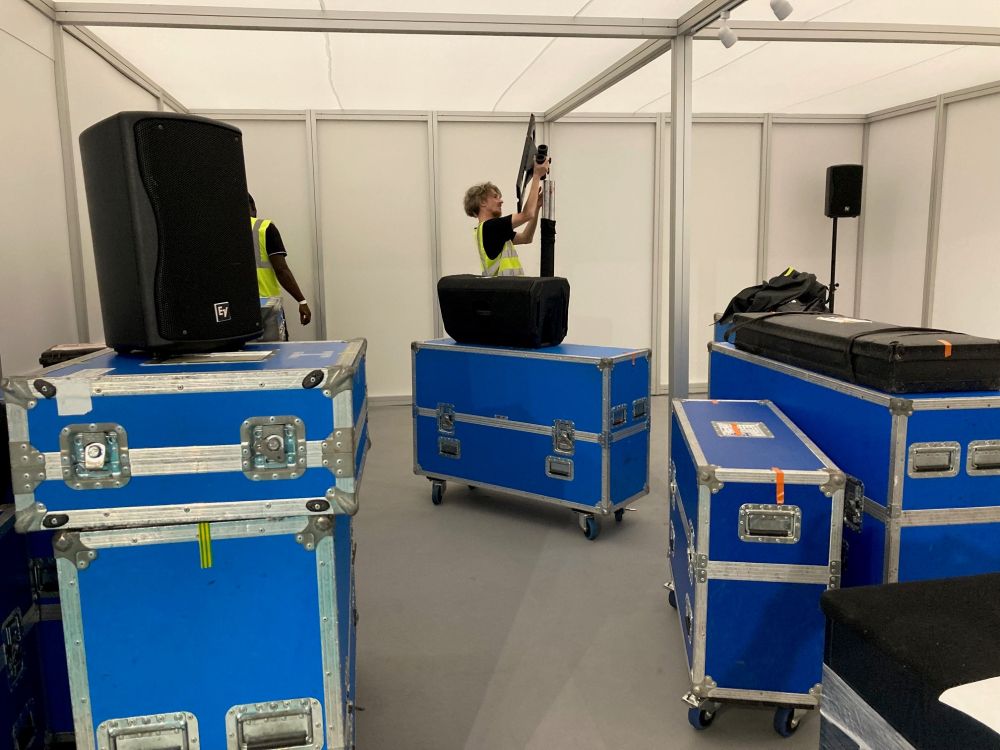 Staff set up some speakers in the seminar theatre. A number of large blue boxes are in the foreground.