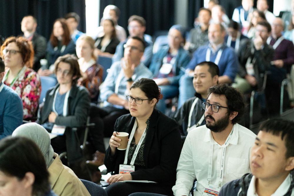 A packed conference audience listens intently to a speaker who is out of shot.