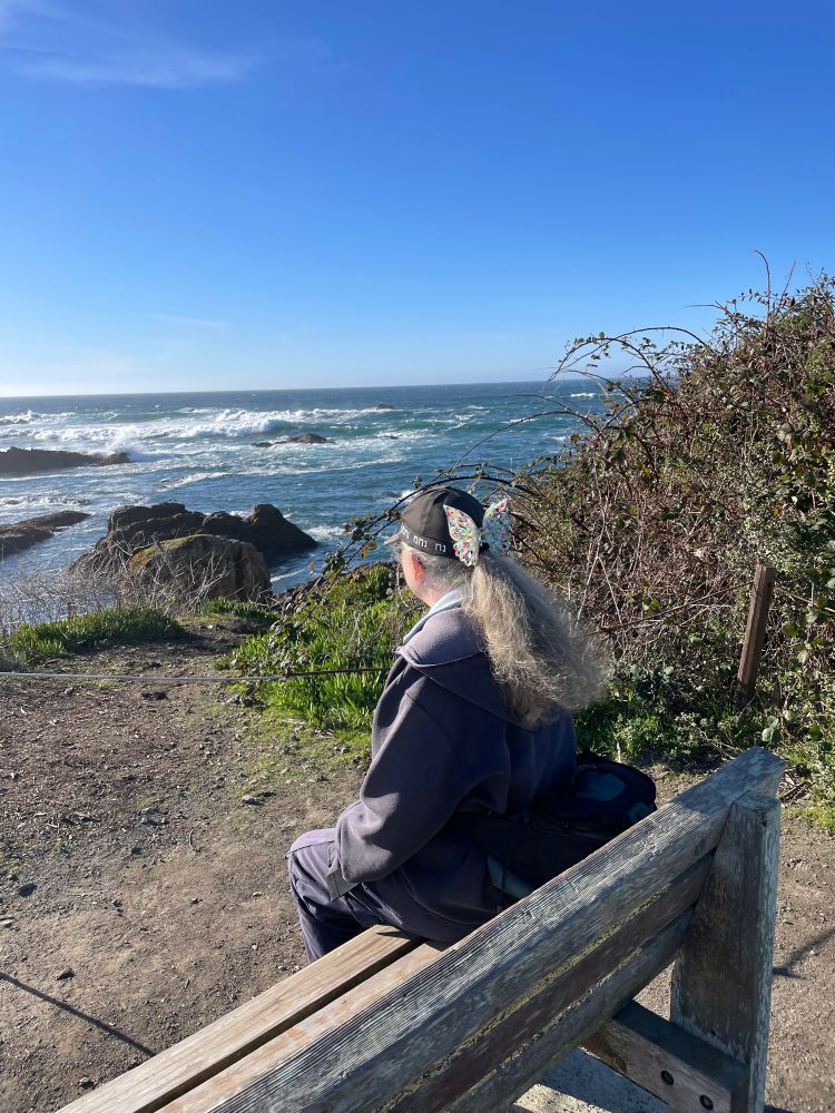 Side view of w woman on a bench overlooking some headlands and ocean. 