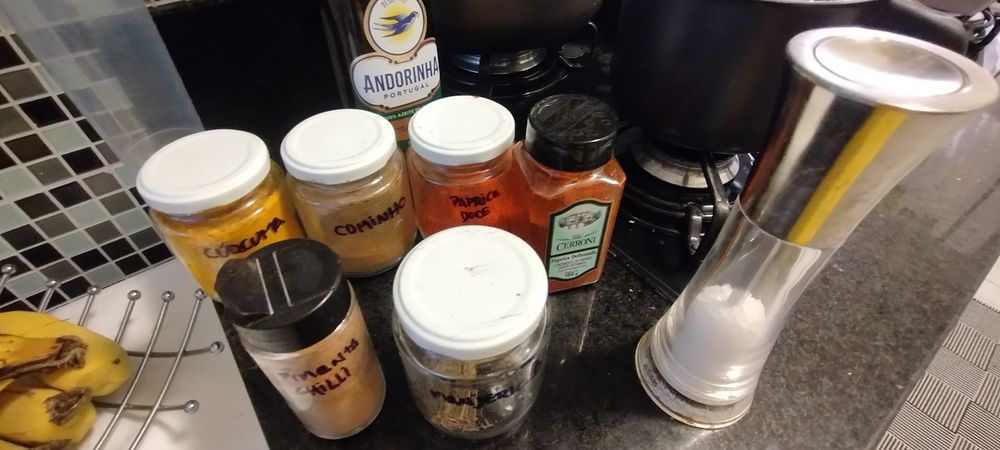 bancada de cozinha com garrafa de azeite, potes de cúrcuma, cominho, páprica doce e defumada, pimenta chilli, manjericão desidratado e sal