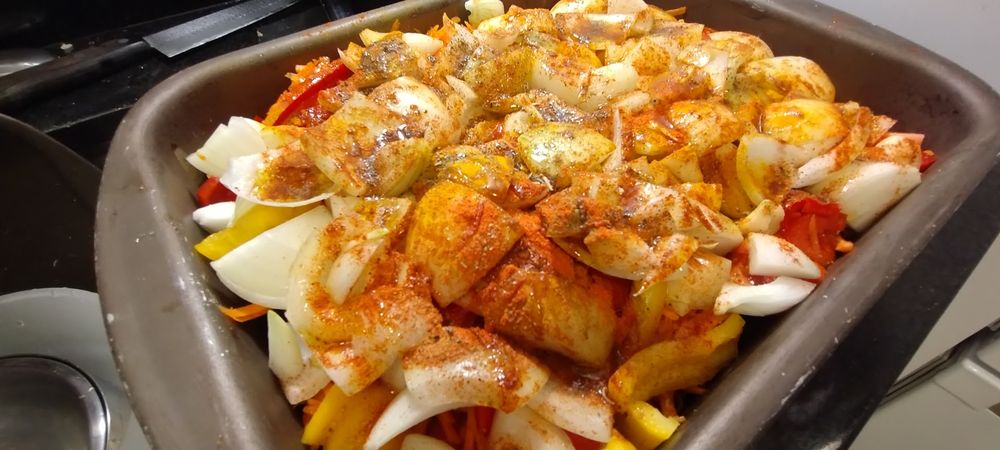 assadeira com legumes picados, condimentos secos e azeite espalhados sobre eles