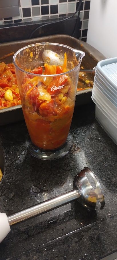 bancada de pia com um copo transparente de acríco com molho de tomate dentro e a haste de um mixer na fente dele