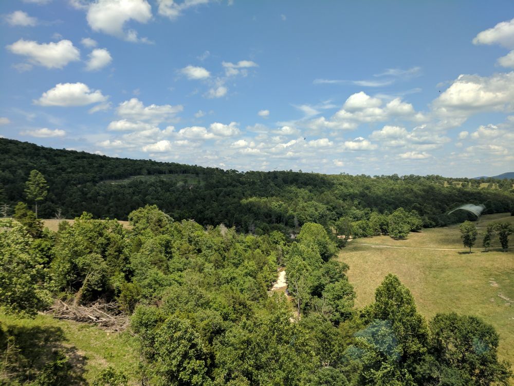 Green, tree covered hills with open blue sky and soft cloud cover.
