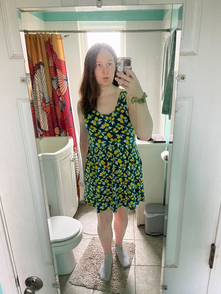 a tall white woman with brown hair wearing a blue dress with a yellow lemon pattern