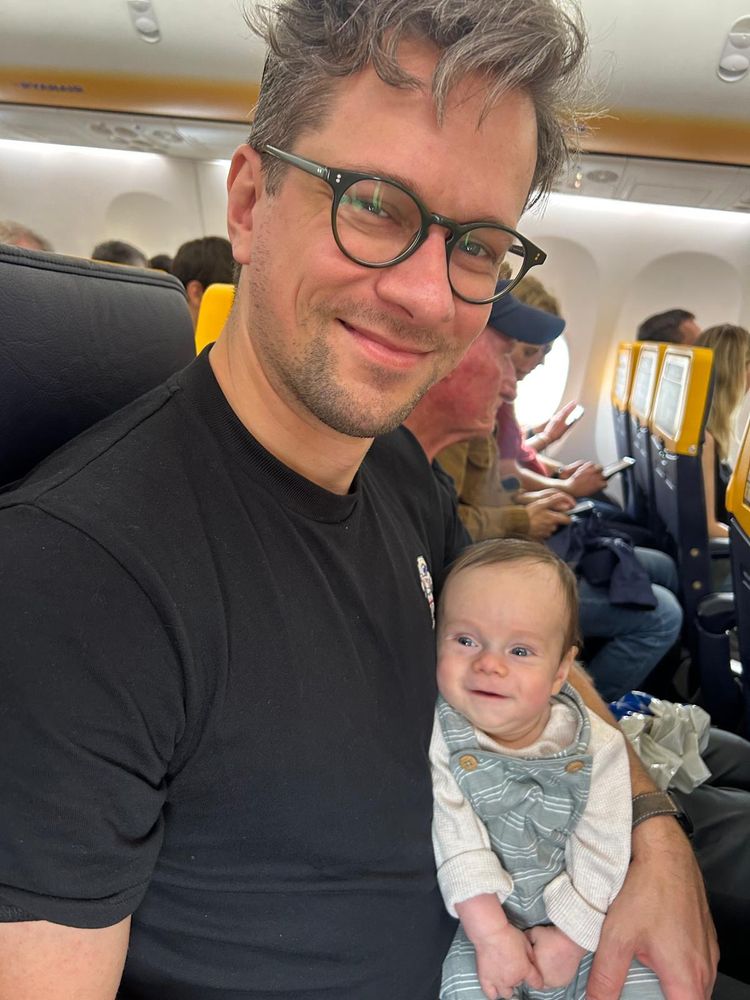 A man sitting inside an airplane. A small child sits on his lap