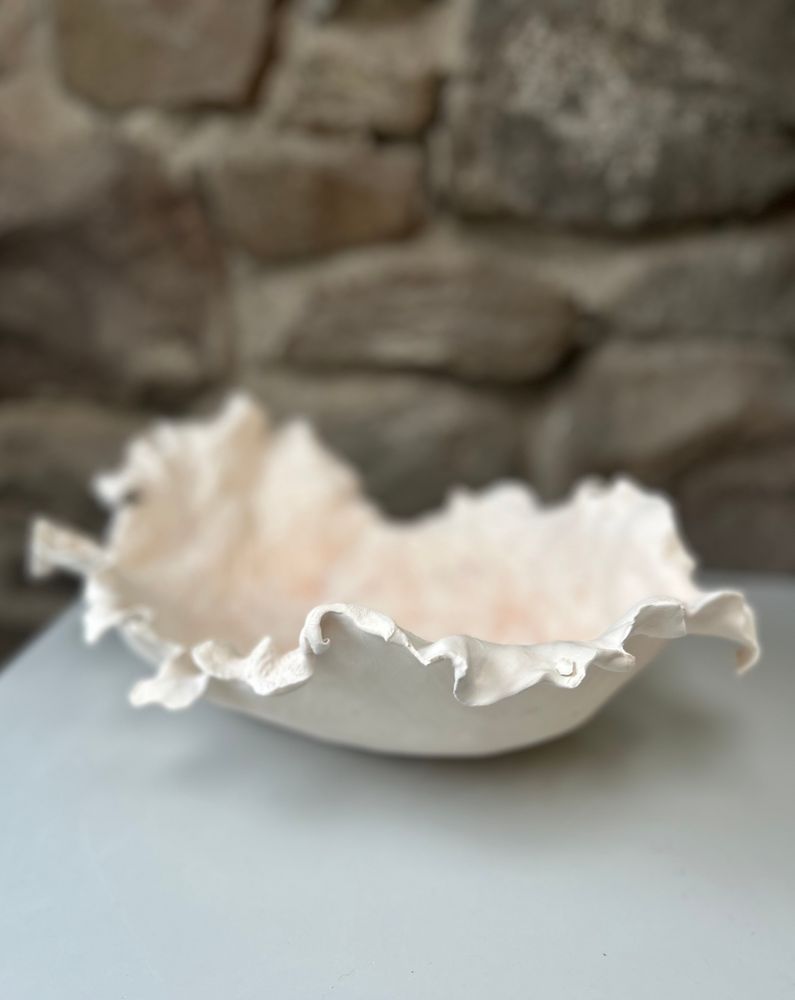 Photographs of an organic, white clay vessel, with fragile, curled edges. Three different angles