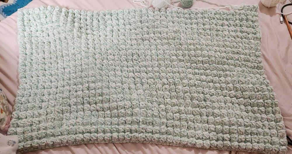 Foto de um cobertor de bebê em ponto pipoca, nas cores branco e verde água