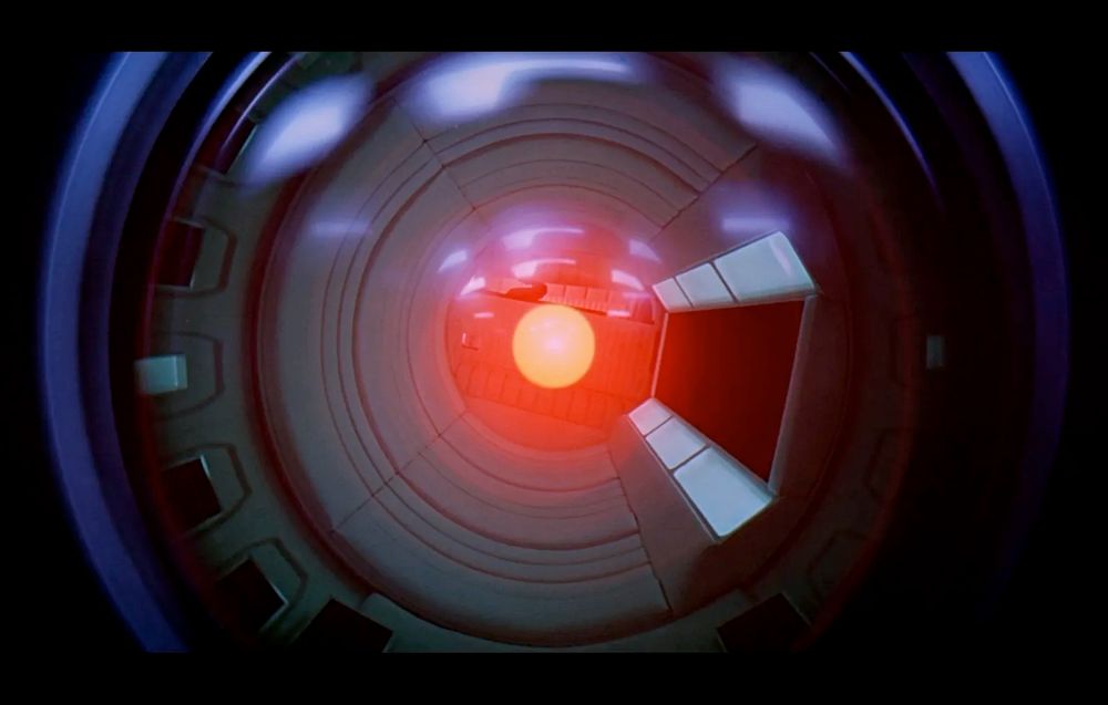 A camera-like lens with glowing red dot in the center representing the "essence" or the eye of antagonist robot/AI "HAL 9000" as seen in the Space Odyssey series