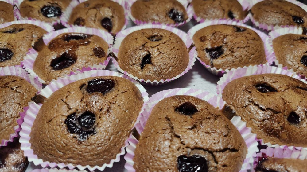 Chocolate muffins with cherries in them, in pink paper cups.