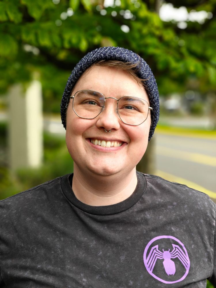 A color photo of an androgynous white  person wearing silver frame glasses and a big smile