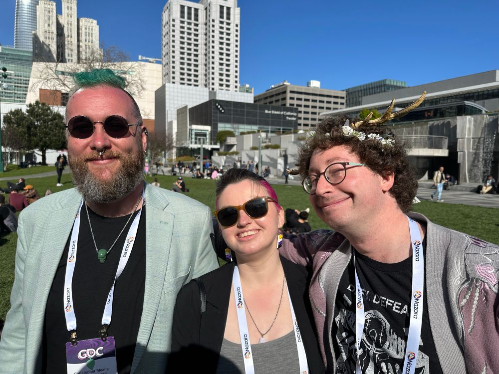 Larysa with pink in their hair is smiling alongside a new and old friend in Yerba Buena park, on the last day, as another friend takes their photo because Larysa remembered their co-founder asked them to take photos and this was now the last opportunity to do so. Thank you co-founder!