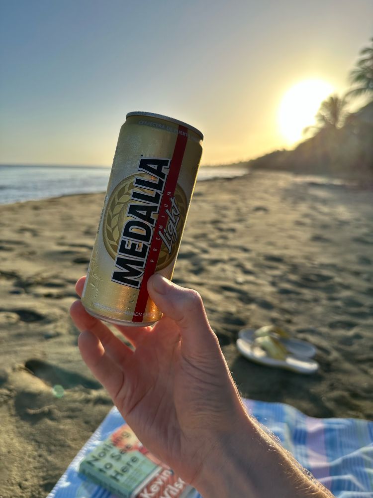 A can of Medalla set against a sunset on a beach. 