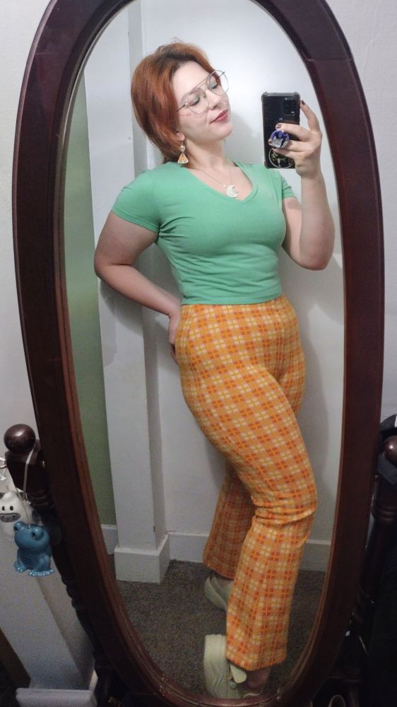 red hair woman taking mirror selfie wearing orange plaid stretchy kick flare pants and a mint green v neck shirt