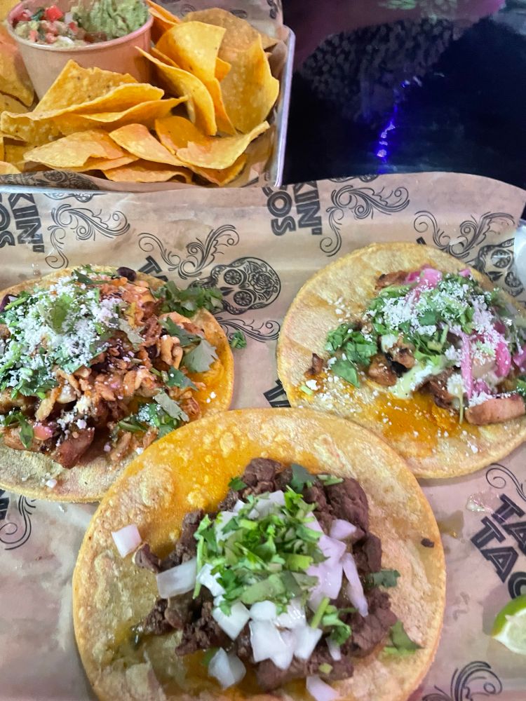 3 tacos with various fillings on a tray with tortilla chips in the background