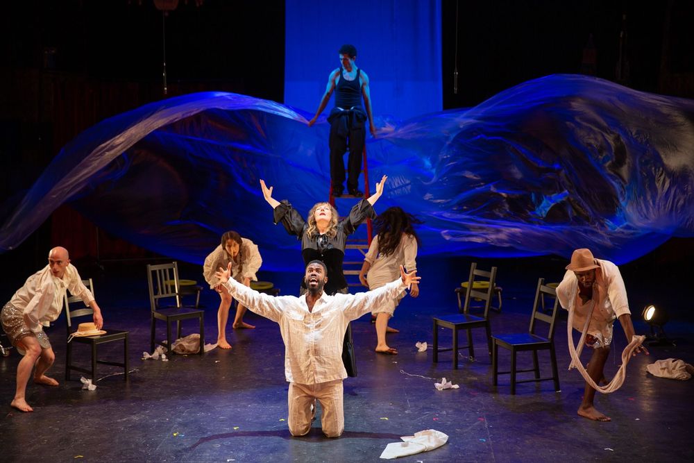 Actors declaim on a dark stage; behind and above them, a man on a ladder waves a huge sheet of blue-lit plastic as if he's flapping gigantic wings