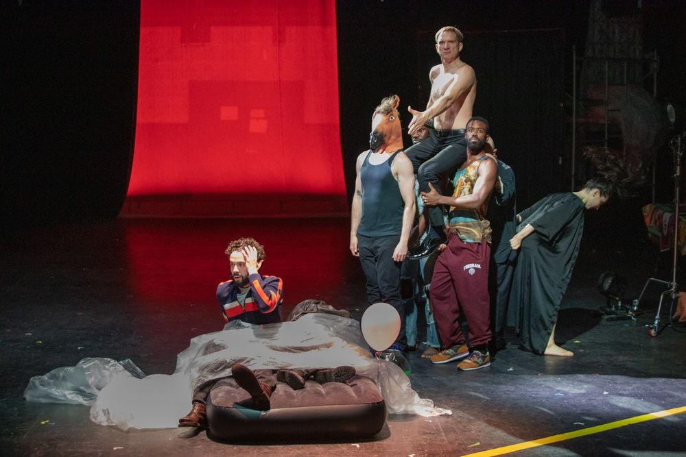A man startles awake on his inflatable mattress, as a nightmare vision of Putin (Andrey Burkovskiy, with his shirt off, riding a "horse" made out of four actors) points a finger-gun at him 