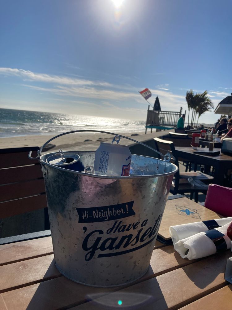 Chilled beers sit on a table that is positioned next to the Atlantic rolling in up the beach in New England. The wind tugs at the flags and the gulls glide overhead.