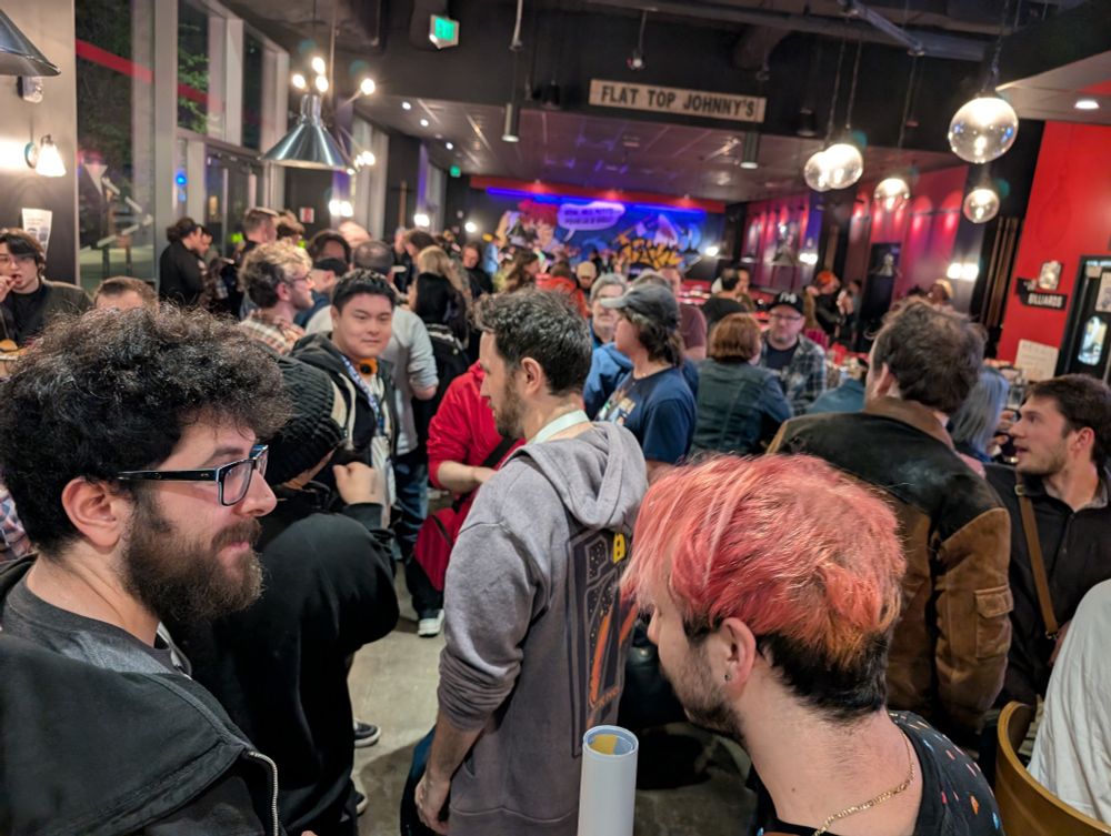 A crowd of people chatting in a bar. There's a sign that reads "Flat Top Johnny's".